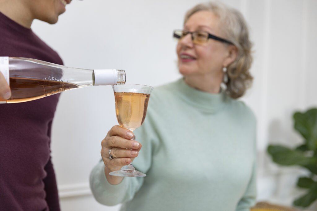 Opiekunka jest częstowana alkoholem przez rodzinę podopiecznego. Trzyma w ręce lampkę z winem.