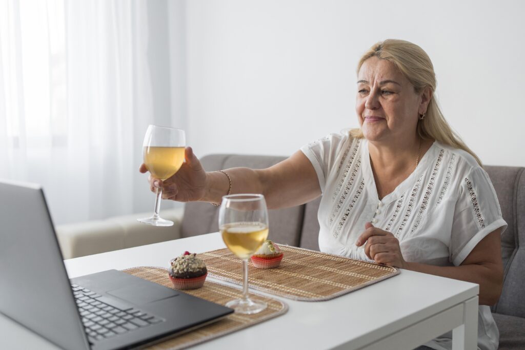 Opiekunka pije wino w przerwie, rozmawiając za pomocą laptopa z rodziną.