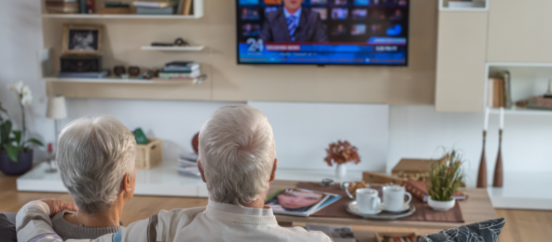Para seniorów siedzi przed telewizorem i ogląda wiadomości.