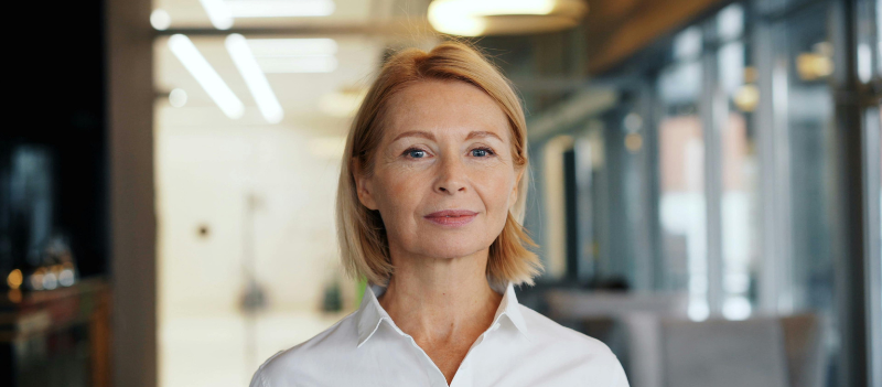 Biuro agencji opieki - kobieta uśmiecha się delikatnie na pierwszym planie.
