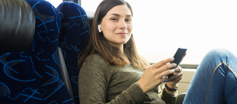 Młoda kobieta jadąca autobusem i słuchająca muzyki przez słuchawki.