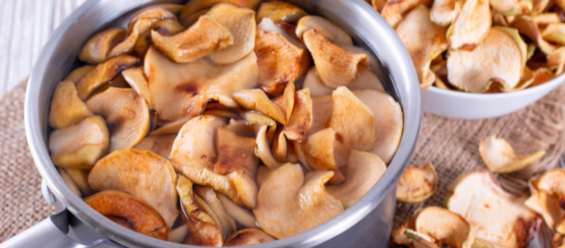 Garnek z gotującym się kompotem z suszonych owoców; na powierzchni widać kawałki jabłek, gruszek i śliwek unoszące się w lekkiej parze.