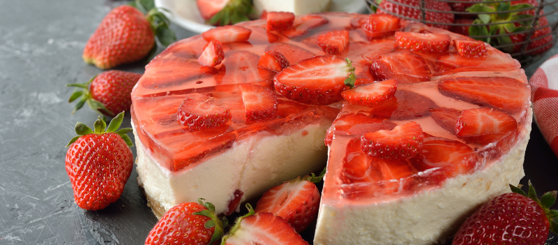 Sernik na zimno z truskawkami i galaretką na jasnym spodzie, udekorowany świeżymi owocami i zalany klarowną truskawkową galaretką.