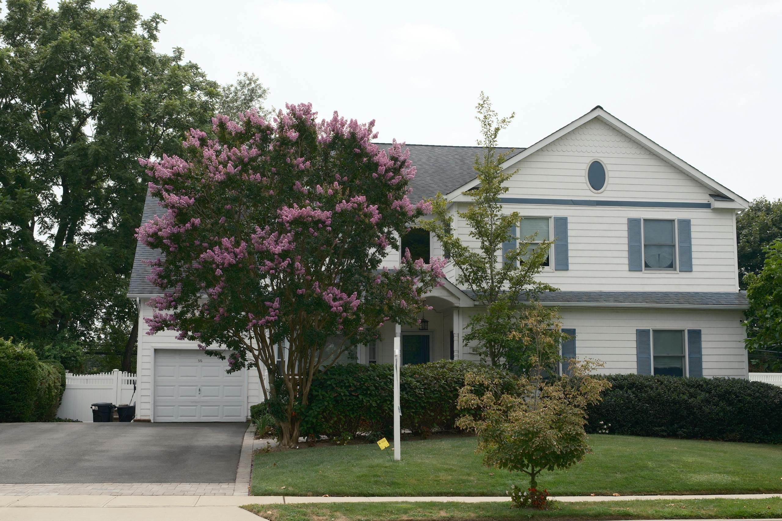 front view of a suburban house with a blooming crape myrtle tree in the garden showcasing lush greenery. 33350018 scaled