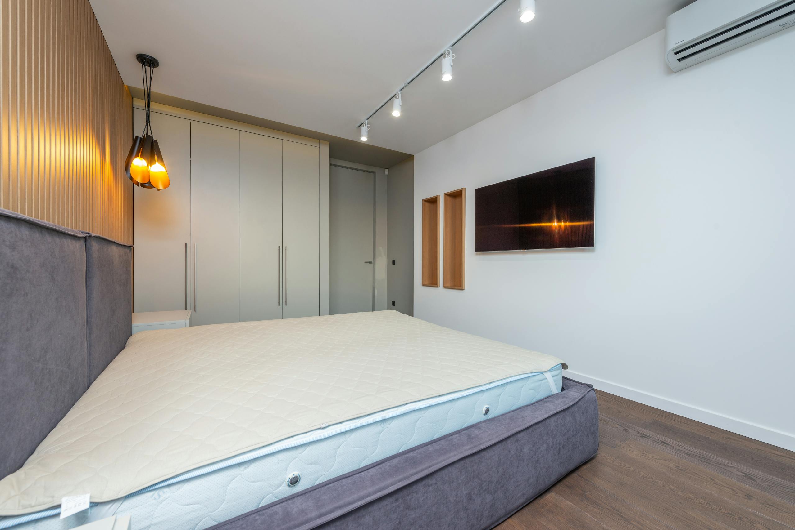 spacious modern bedroom featuring a gray bed and wall mounted tv with ambient lighting. 8089073 scaled