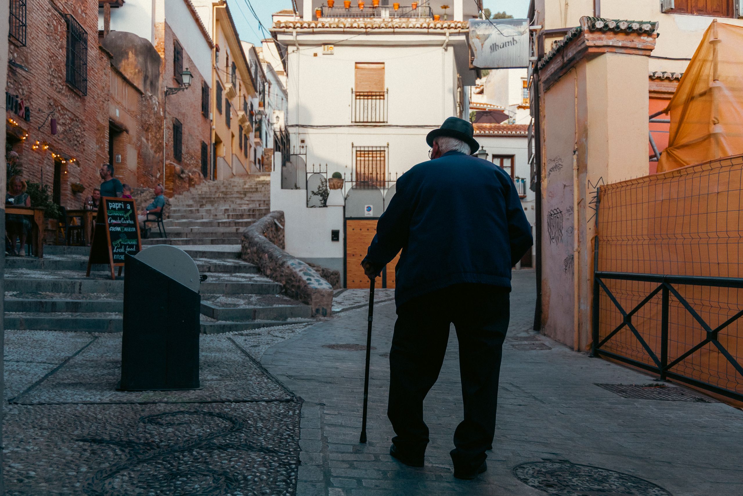 A candid view of an elderly man with a cane strolling through the scenic streets of Granada, Spain.
