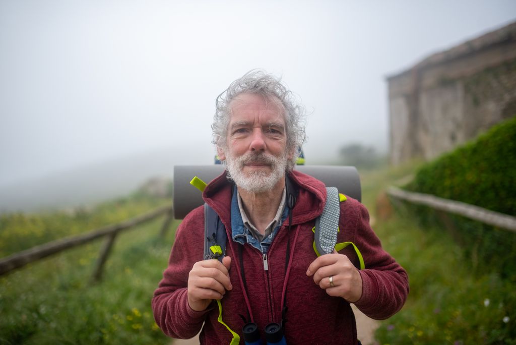 Elderly man hiking with backpack on a misty trail in Portugal, capturing the spirit of outdoor adventure.